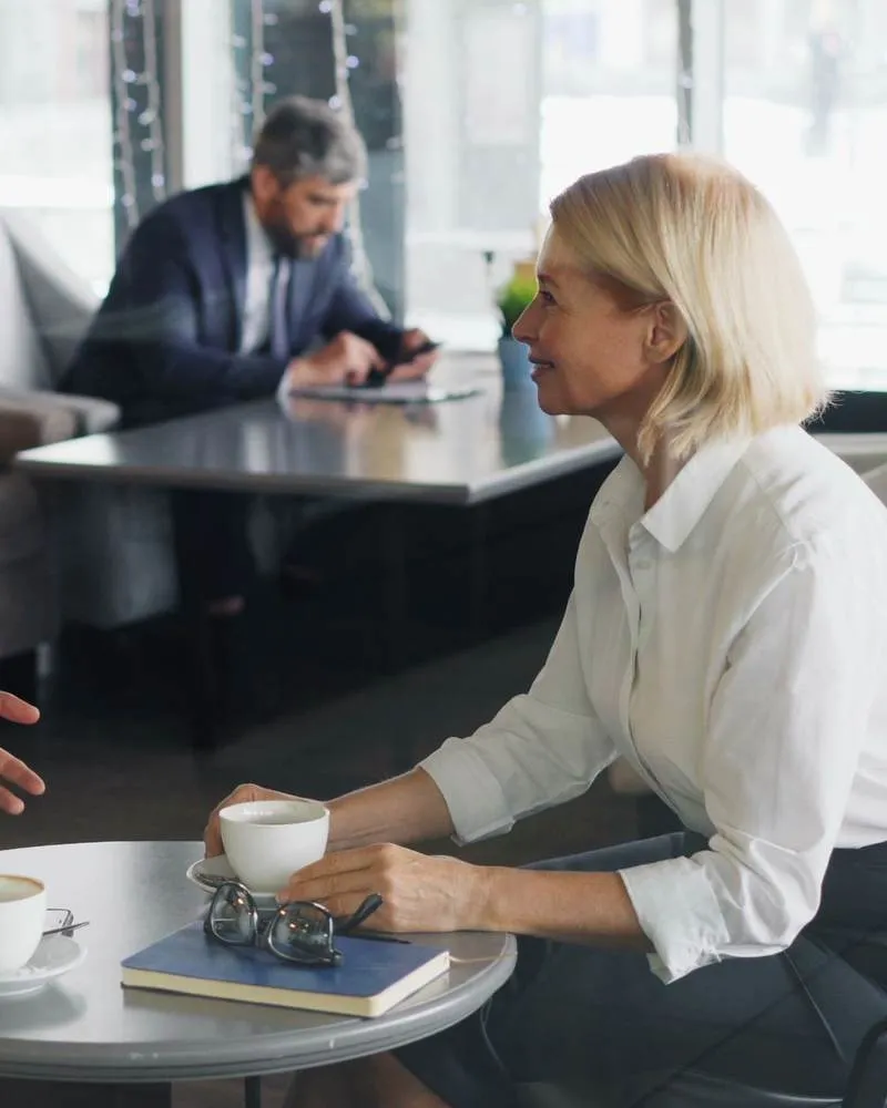 Une femme écoute attentivement son interlocuteur autour d'un café, dans un cadre calme et lumineux
