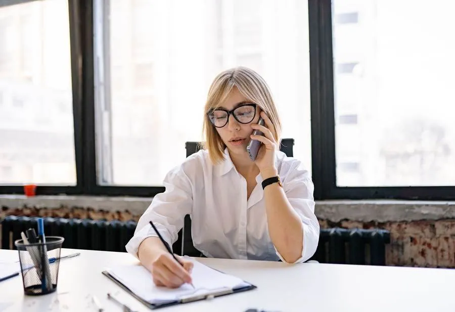 Une personne au téléphone prenant des notes sur un bloc-papier, dans un bureau lumineux